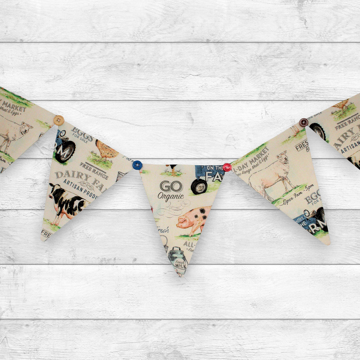 A bunting banner with triangular flags printed with vintage-style dairy farm illustrations and text, hung on a white wood plank background.