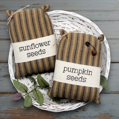 Two striped fabric feed sack style bags labeled 'sunflower seeds' and 'pumpkin seeds' on a white basket.
