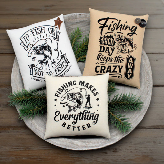 Three fishing-themed pillows on a wooden surface with pine branches.