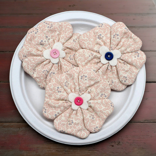 Floral-patterned fabric flowers with buttons on a white plate against a wooden background