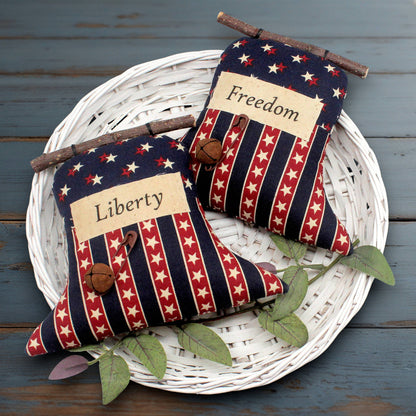 Set of two primitive liberty bell ornaments with labels that read Freedom and Liberty, decorated with rusty safety pins and bells