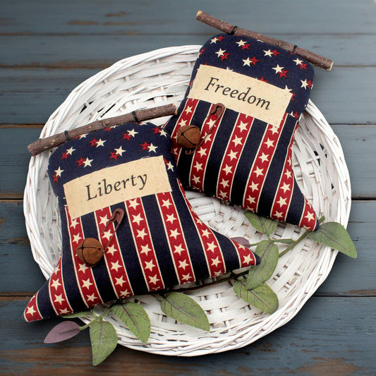 Set of two primitive liberty bell ornaments with labels that read Freedom and Liberty, decorated with rusty safety pins and bells