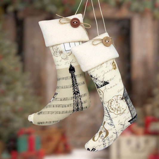 Two fabric Christmas stockings hanging from strings, decorated with Eiffel Tower and vintage-style handwriting patterns in black on a cream background, with cream cuffs and wooden button accents.