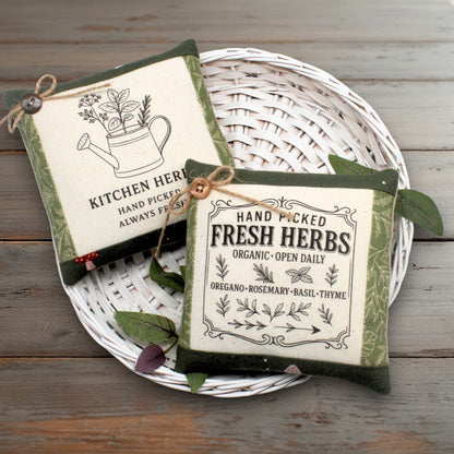 Set of two fabric mini pillow bowl fillers with garden herb designs and text, displayed on a white basket against a wooden table