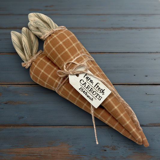 Plush carrots wrapped in brown checkered fabric with a tag on a wooden surface