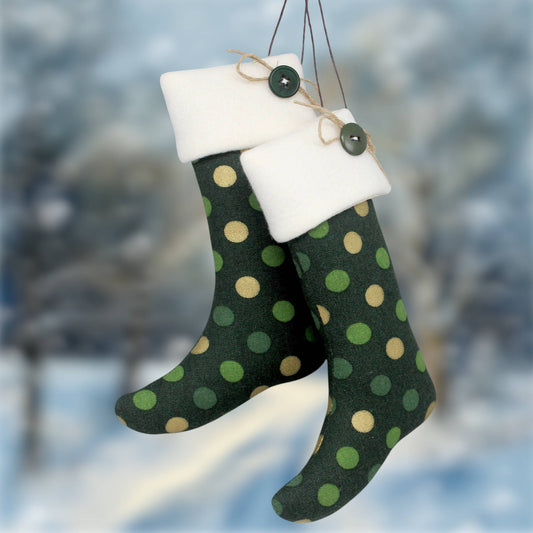 Two hanging Christmas stockings with dark green and olive polka dots, white fleece cuffs, and green buttons, set against a blurred snowy outdoor background.