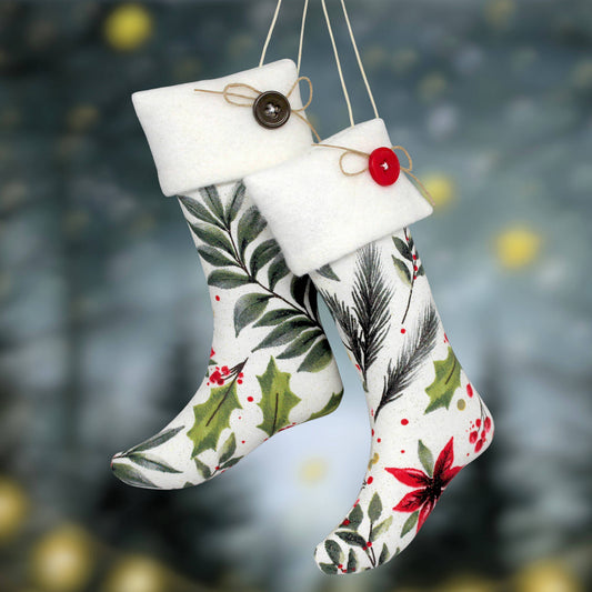 Two Christmas stocking ornaments with poinsettia and holiday greenery designs hanging against a blurred festive background. One stocking has a white cuff with a brown button and twine, and the other has a white cuff with a red button and twine.