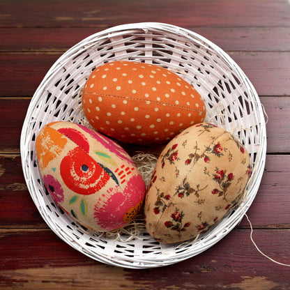 Decorative fabric eggs in a white basket on a wooden surface
