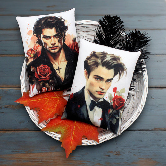 Two pillows with handsome young male vampires with red roses on a wooden surface.