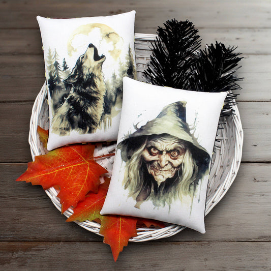 Two decorative pillows with wolf and hooded old witch designs on a wooden surface with autumn leaves.