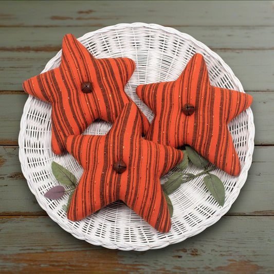 Set of three fabric stars in orange fabric with black stripes and rusty bells in the centers