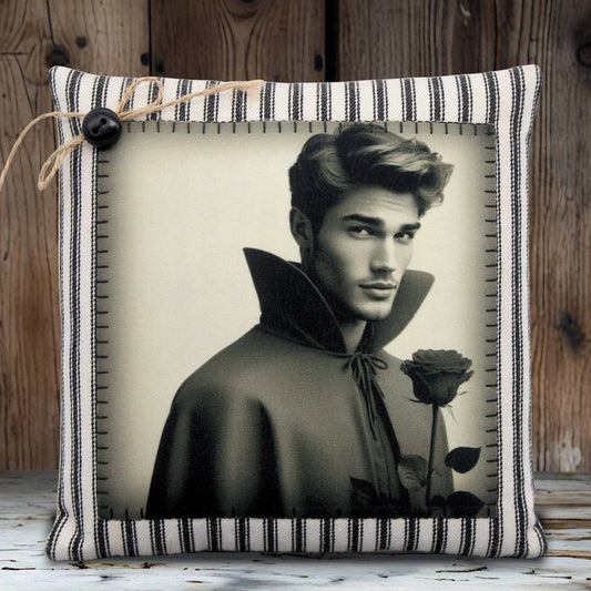 Decorative pillow with a black and white photo of a handsome young vampire in a cape holding a rose, on a striped fabric background.