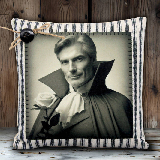 Decorative pillow with a black and white portrait of a handsome vampire in a cape and a rose, on a striped fabric background.