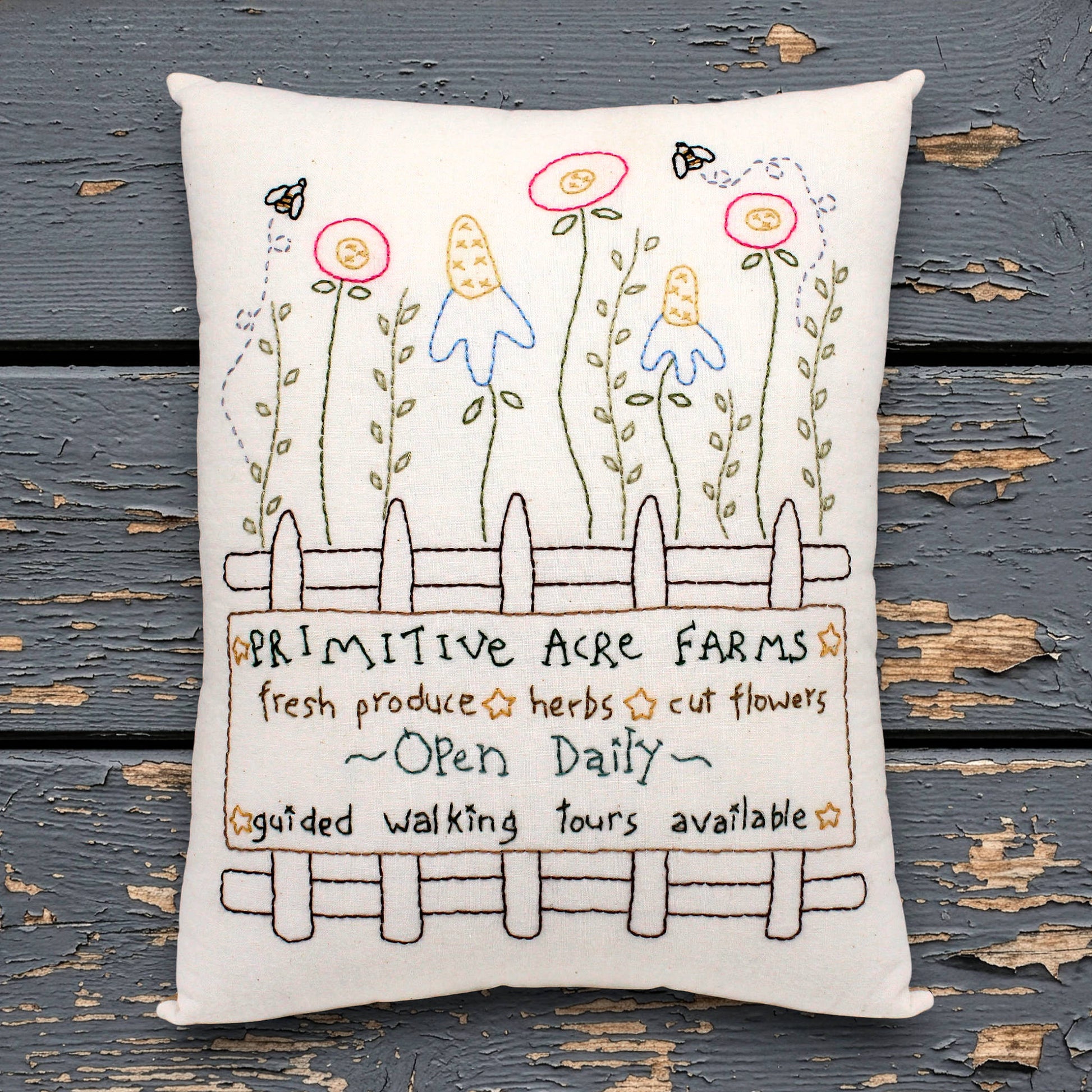 Decorative pillow with hand-stitched design of flowers and text on a wooden surface