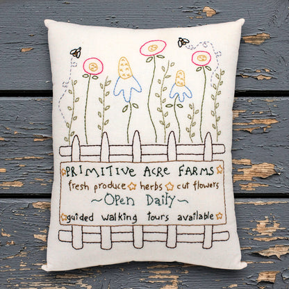 Decorative pillow with hand-stitched design of flowers and text on a wooden surface