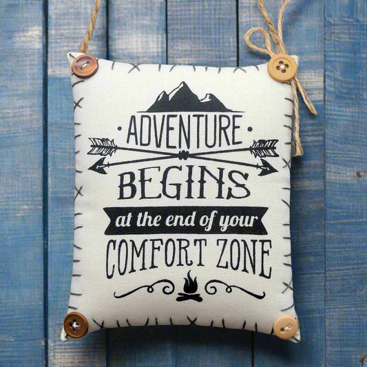 Decorative sign with 'Adventure Begins at the End of Your Comfort Zone' text on a blue wooden background