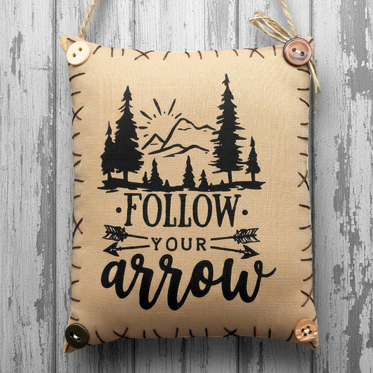 Decorative pillow with nature-themed design and 'Follow Your Arrow' text on a wooden surface.