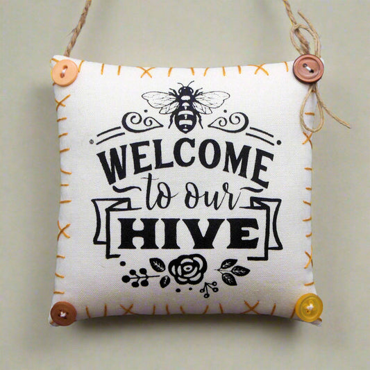 Decorative pillow with 'Welcome to our Hive' text and bee design on a plain background