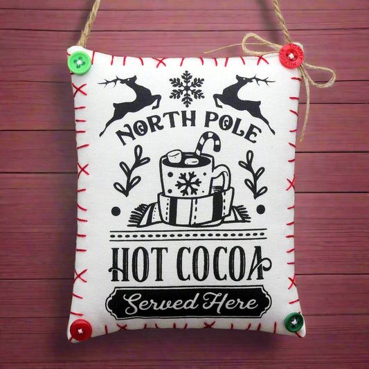 Decorative sign with 'North Pole Hot Cocoa Served Here' text on a wooden background