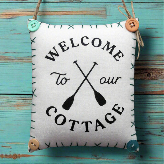 Decorative sign with 'Welcome to our Cottage' text and oar graphics on a wooden background