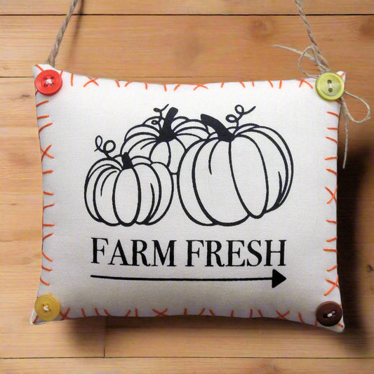 Decorative pillow with pumpkins and 'Farm Fresh' text on a wooden surface