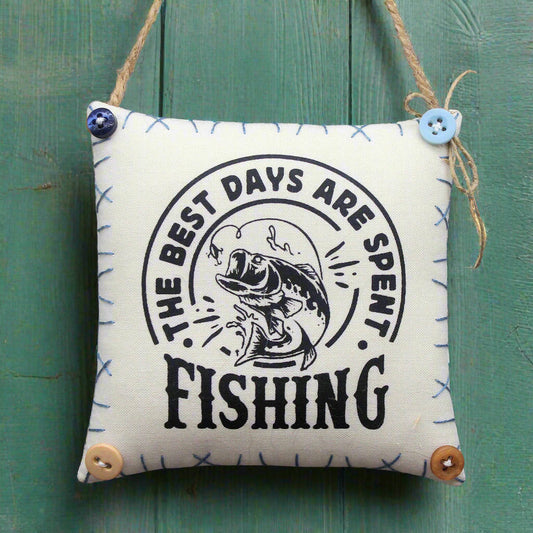 Small pillow with 'The best days are spent fishing' text and fish illustration on a green wooden background