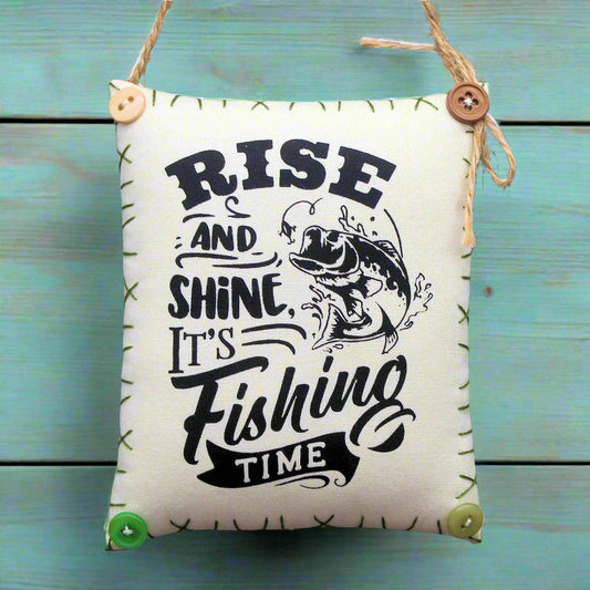 Decorative sign with 'Rise and Shine, It's Fishing Time' text on a wooden background