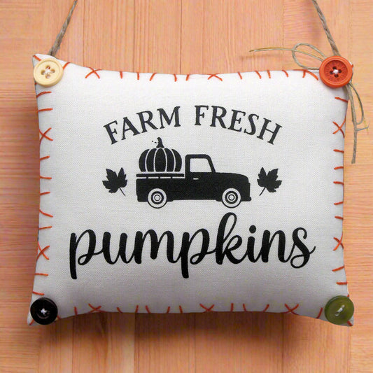 Decorative pillow with 'Farm Fresh Pumpkins' text and truck graphic on a wooden surface