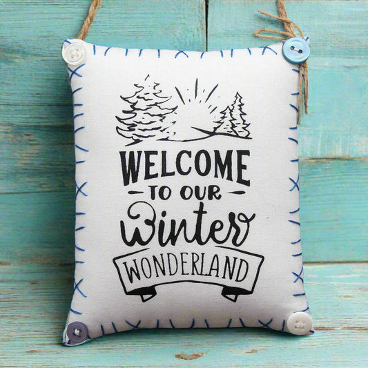 Decorative pillow with 'Welcome to our winter wonderland' text on a wooden surface