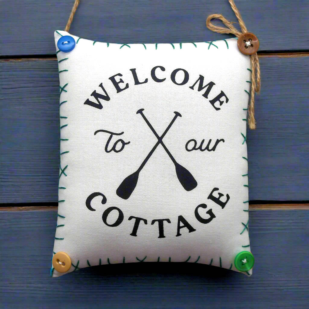 Decorative sign with 'Welcome to our Cottage' text and oar design on a blue wooden background.