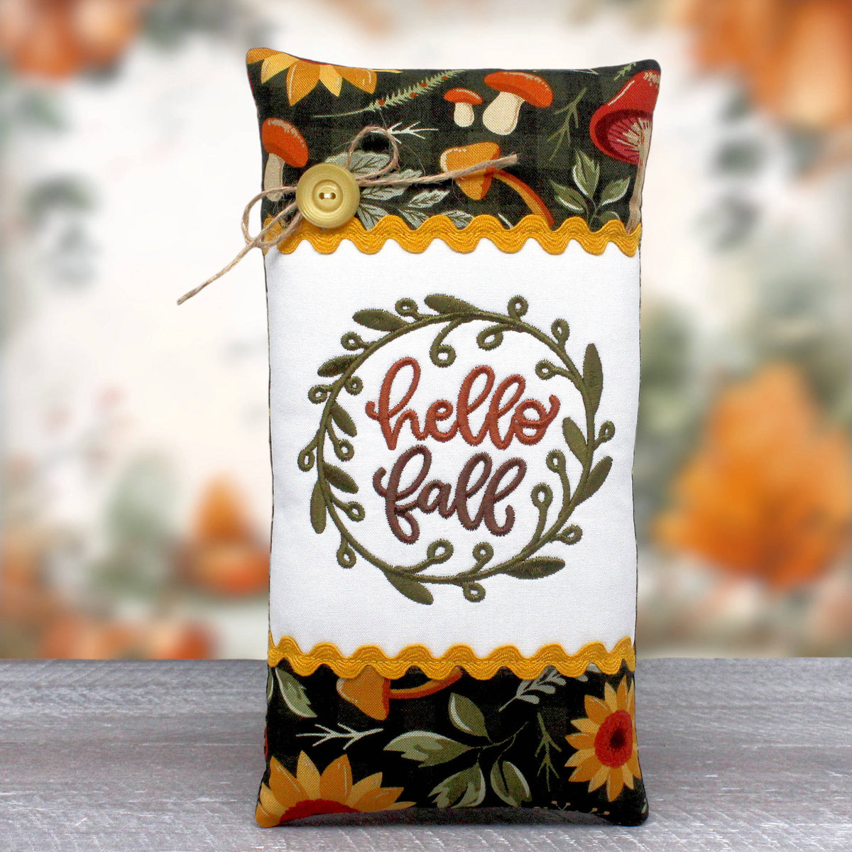 Small pillow tuck or bowl filler embroidered with the greeting 'hello fall' and trimmed with rick rack and colorful fall fabric.