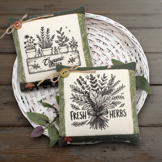 Set of two mini pillow bowl fillers with country primitive herb garden designs displayed on a white basket against a wooden background