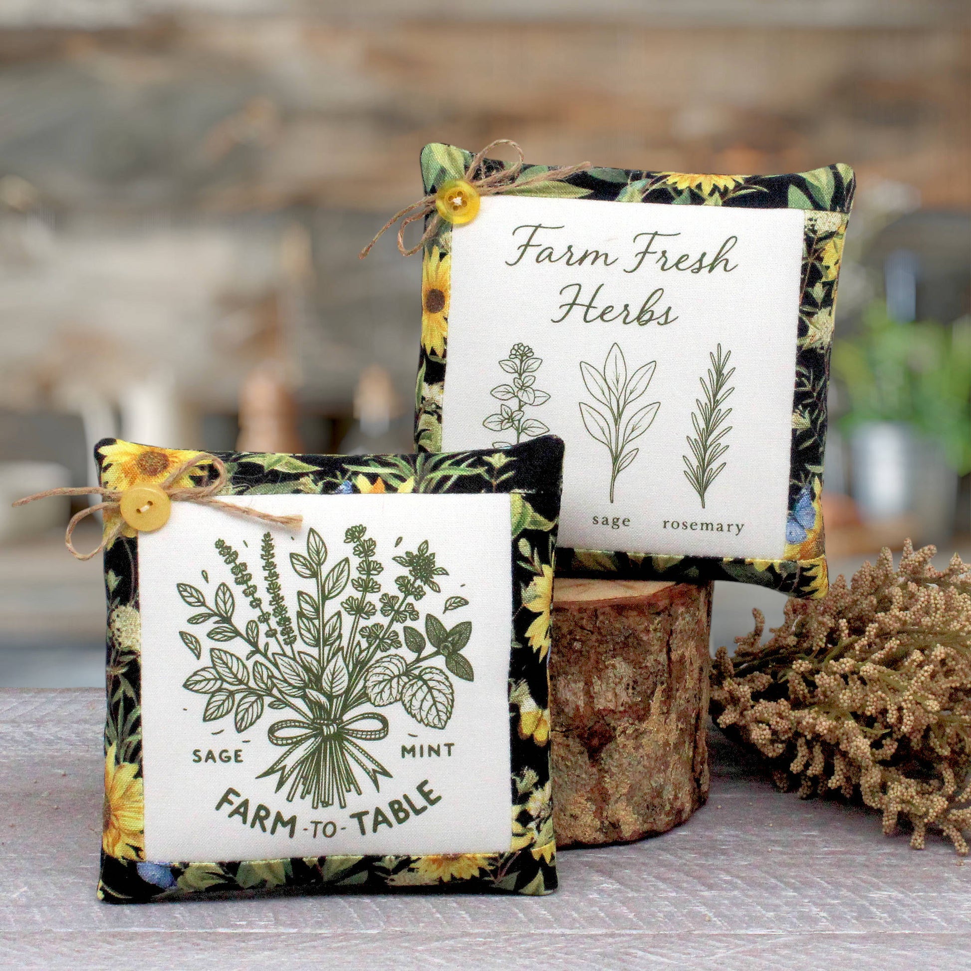 Two square fabric herb-themed mini pillows displayed on a rustic wooden surface. One pillow in front reads 'Farm to Table' with sage, mint, and rosemary illustrations, and the back pillow reads 'Farm Fresh Herbs' with botanical drawings.