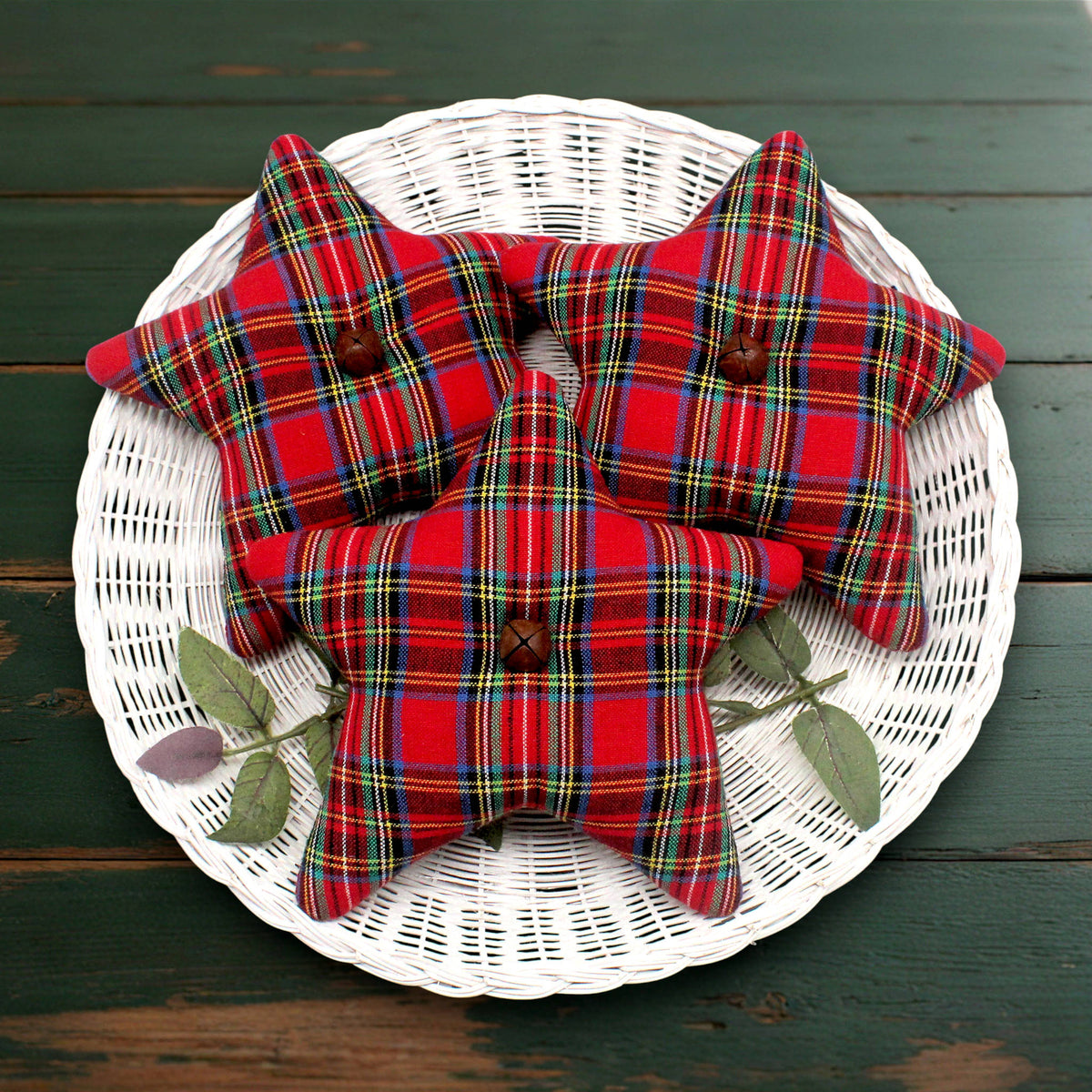 Three star fabric bowl fillers in red tartan plaid fabric with wooden button details, arranged on a white wicker plate over a dark green wooden surface.