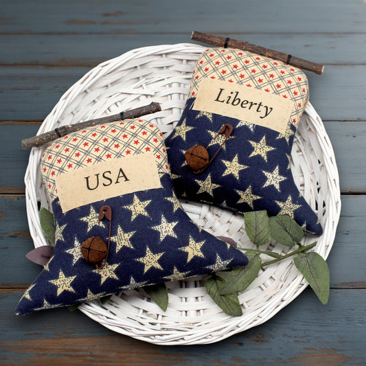 Set of two primitive liberty bell ornaments with labels that read USA and Liberty, decorated with rusty bells and safety pins