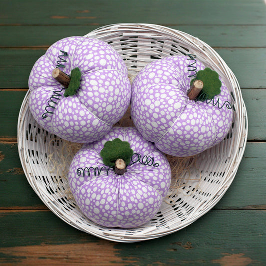 Three purple patterned pumpkins in a white wicker basket on a wooden surface.
