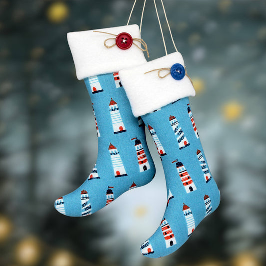 Two blue Christmas stockings with a lighthouse pattern, white fleece cuffs, and decorative buttons, hanging against a blurred festive background.