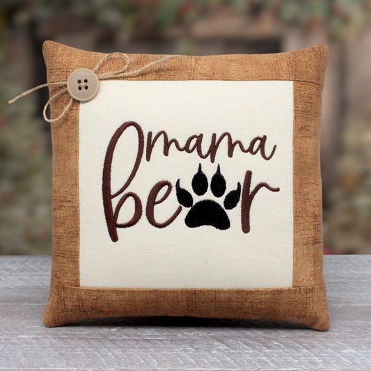 Small pillow tuck or bowl filler embroidered with the words 'mama bear' with a bear paw replacing the A in the word bear.  The center panel is trimmed with a light brown cotton print fabric.