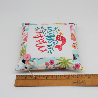 A square fabric pillow with a colorful mermaid-themed print and the words 'make a splash' in stylized script, shown on a white background with a wooden ruler below for scale.