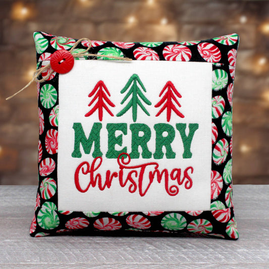 Small pillow tuck or bowl filler embroidered with "Merry Christmas" alongside a few minimalist trees.  The center panel is trimmed with a fabric print with peppermint candy wheels on a black background.