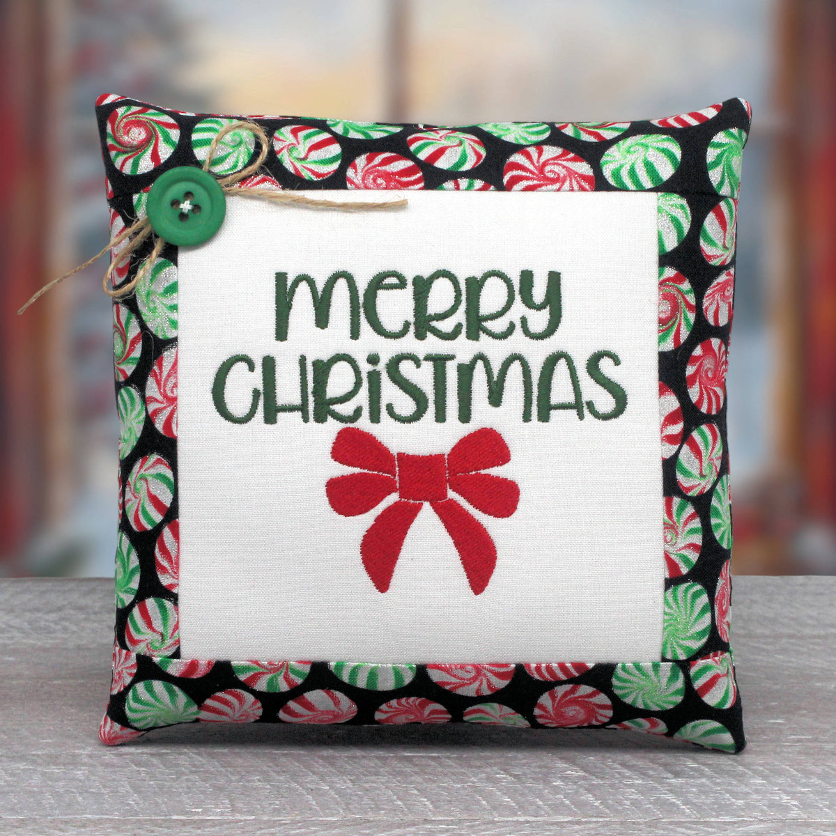 Small embroidered pillow embroidered with the words "Merry Christmas" and a red bow