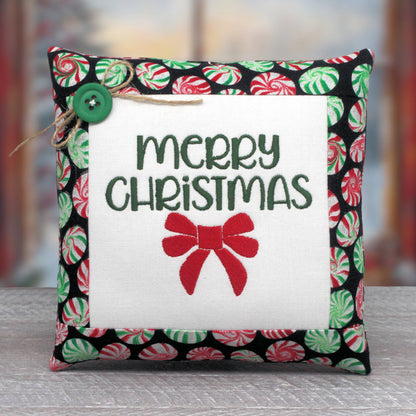 Small embroidered pillow embroidered with the words "Merry Christmas" and a red bow