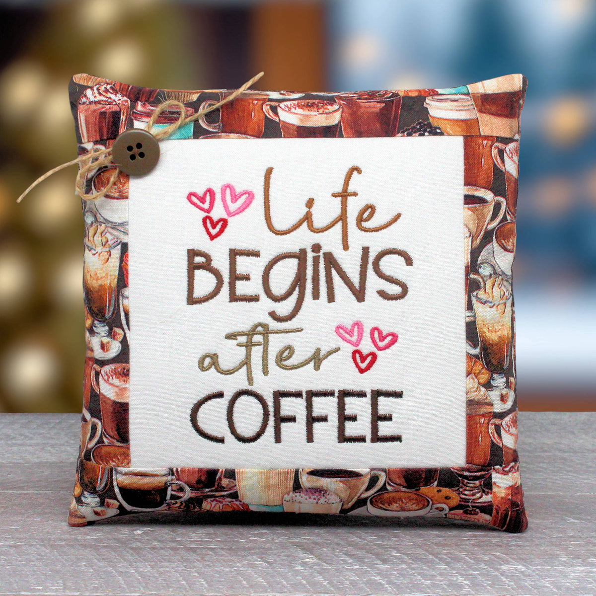 Small pillow tuck or bowl filler embroidered with 'life begins after coffee' with some pink hearts.  The center panel is trimmed with fabric that has a coffee-themed design.