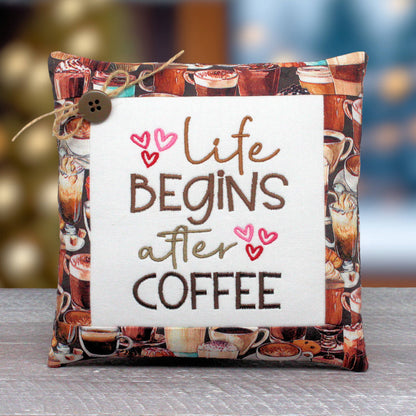 Small pillow tuck or bowl filler embroidered with 'life begins after coffee' with some pink hearts.  The center panel is trimmed with fabric that has a coffee-themed design.