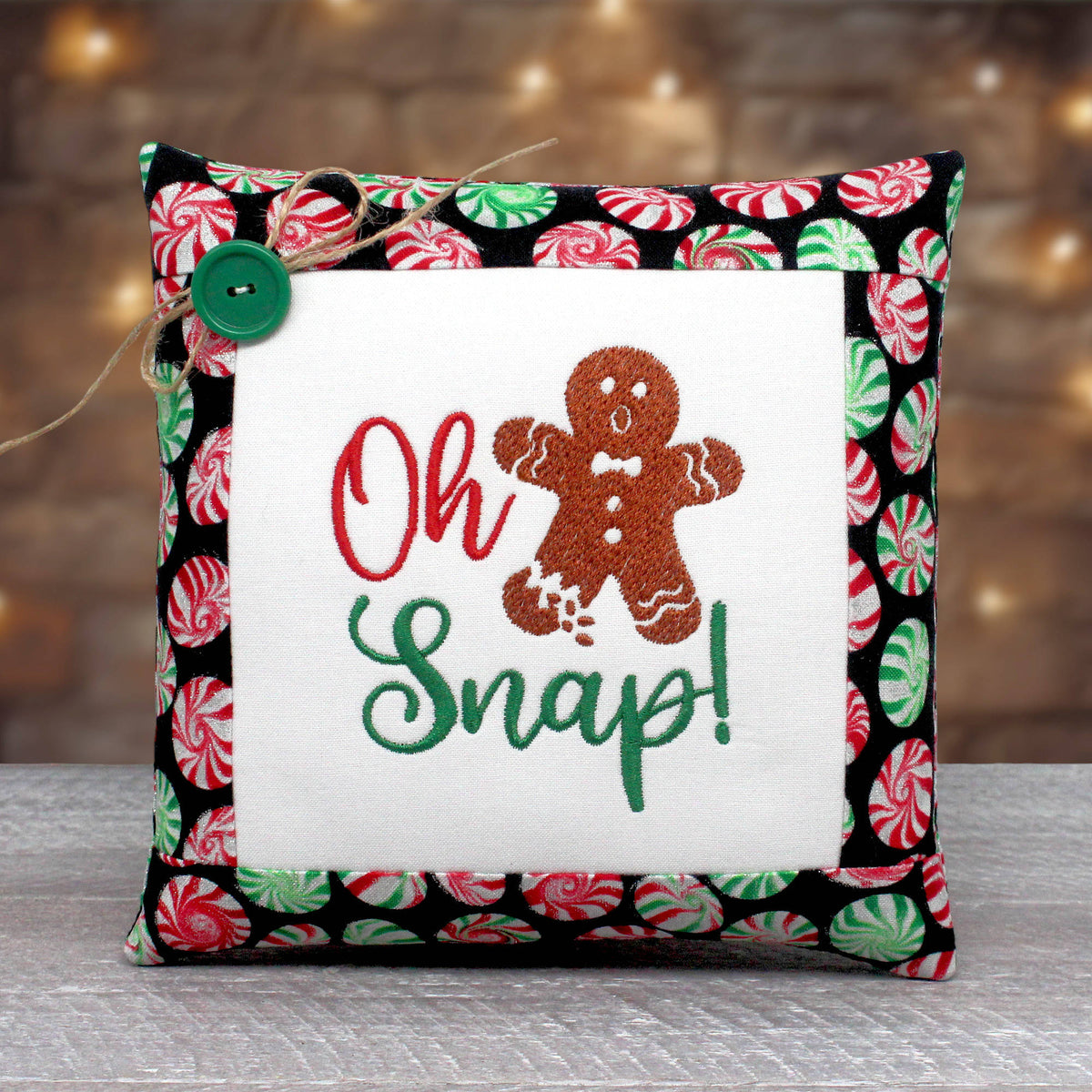 A square decorative throw pillow with a festive holiday design. The center features a white fabric panel with embroidered text reading 'Oh Snap!' in red and green, alongside a brown gingerbread man.
