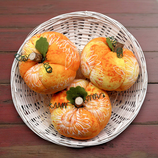 Decorative fabric pumpkins with white patterns on a wicker plate.