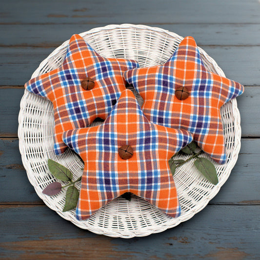 Three star homespun fabric bowl fillers in orange, blue, and white plaid fabric, arranged on a white wicker plate over a dark blue wooden surface.