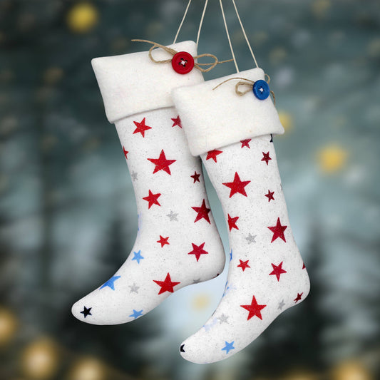Two Christmas stockings hanging side by side, decorated with red, blue, and silver glitter stars. The stockings have white fleece cuffs and are suspended by twine with decorative buttons.