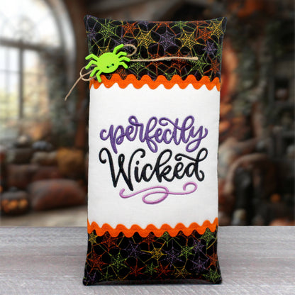 Elongated pillow tuck or bowl filler has a center panel embroidered with 'perfectly wicked.' The center panel is trimmed with rick rack and Halloween-themed print fabric.