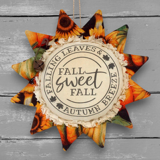 A fabric sunflower hanging ornament with autumn-themed patterns, featuring a printed center that reads 'FALL sweet FALL' and 'FALLING LEAVES & AUTUMN Breeze.'.